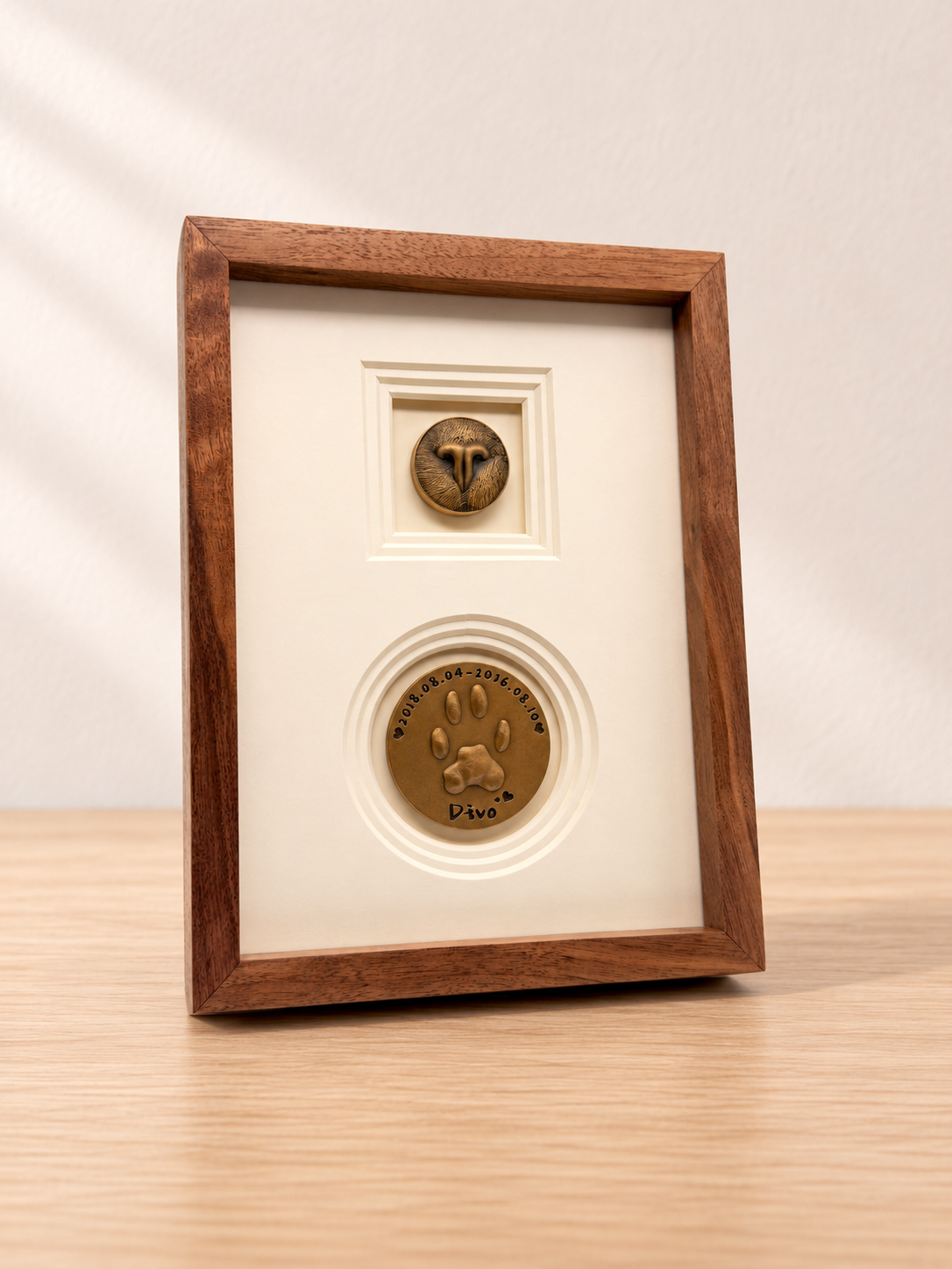 A tall wooden frame with nose-print and paw-print discs on a pale oak table against a cream wall.